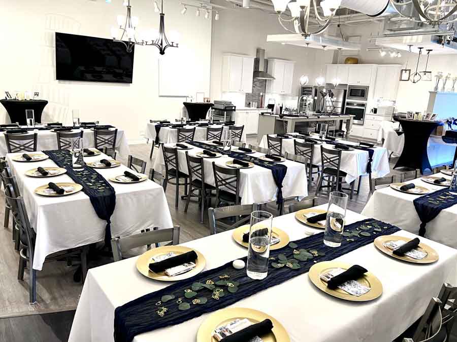 A banquet room set for events and rehearsals with white linens and navy blue table runners.